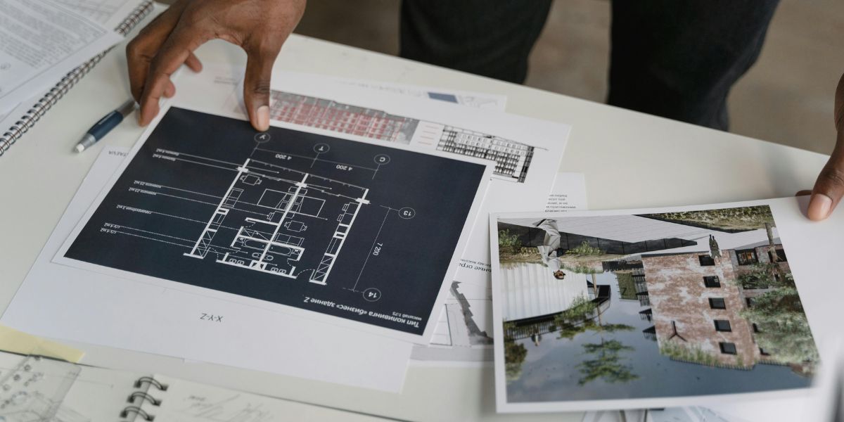 A person holding a black and white architectural blueprint and a full-color photo of a modern brick and glass building