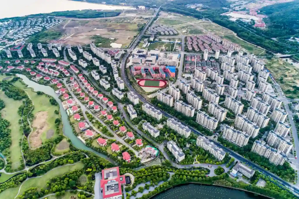 Bird's-eye view of a modern residential area with high-rise apartments, red-roofed houses, a school, and a winding river.