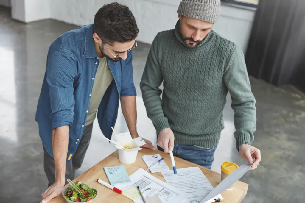 Two coworkers reviewing documents and plans together at a table in an office setting.