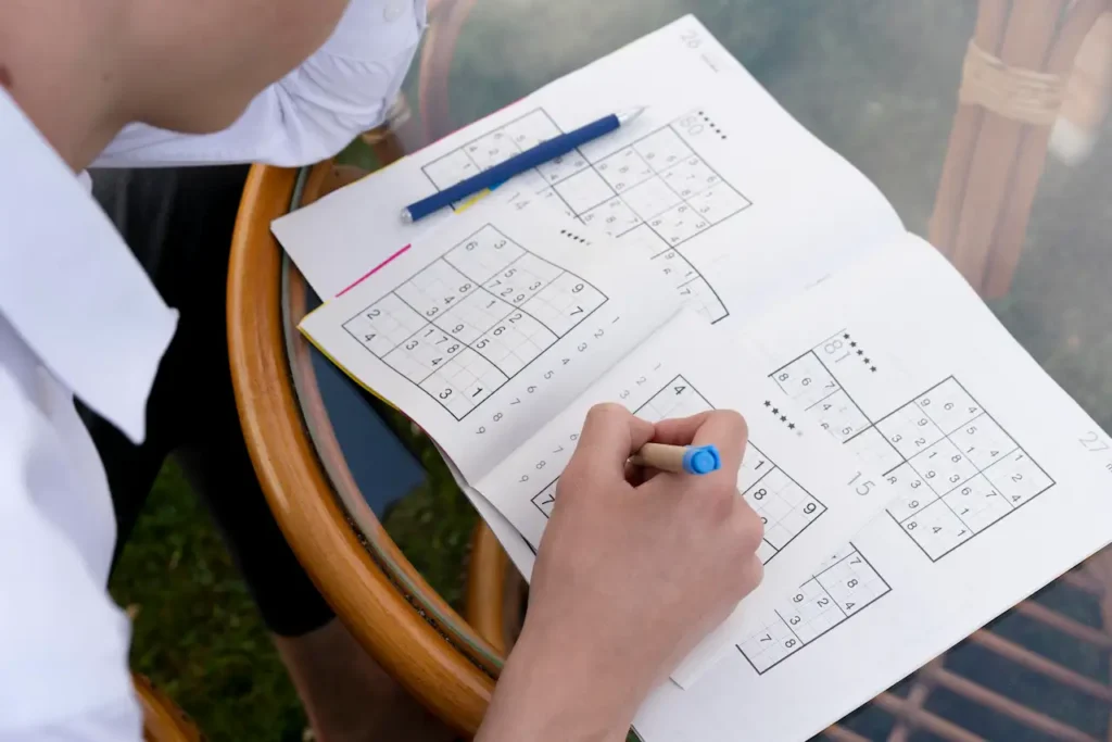 Person solving Sudoku puzzles on paper with a pen at a table.
