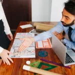 Architect and client reviewing a site plan layout with drawings and tools to discuss design changes and avoid costly revisions.