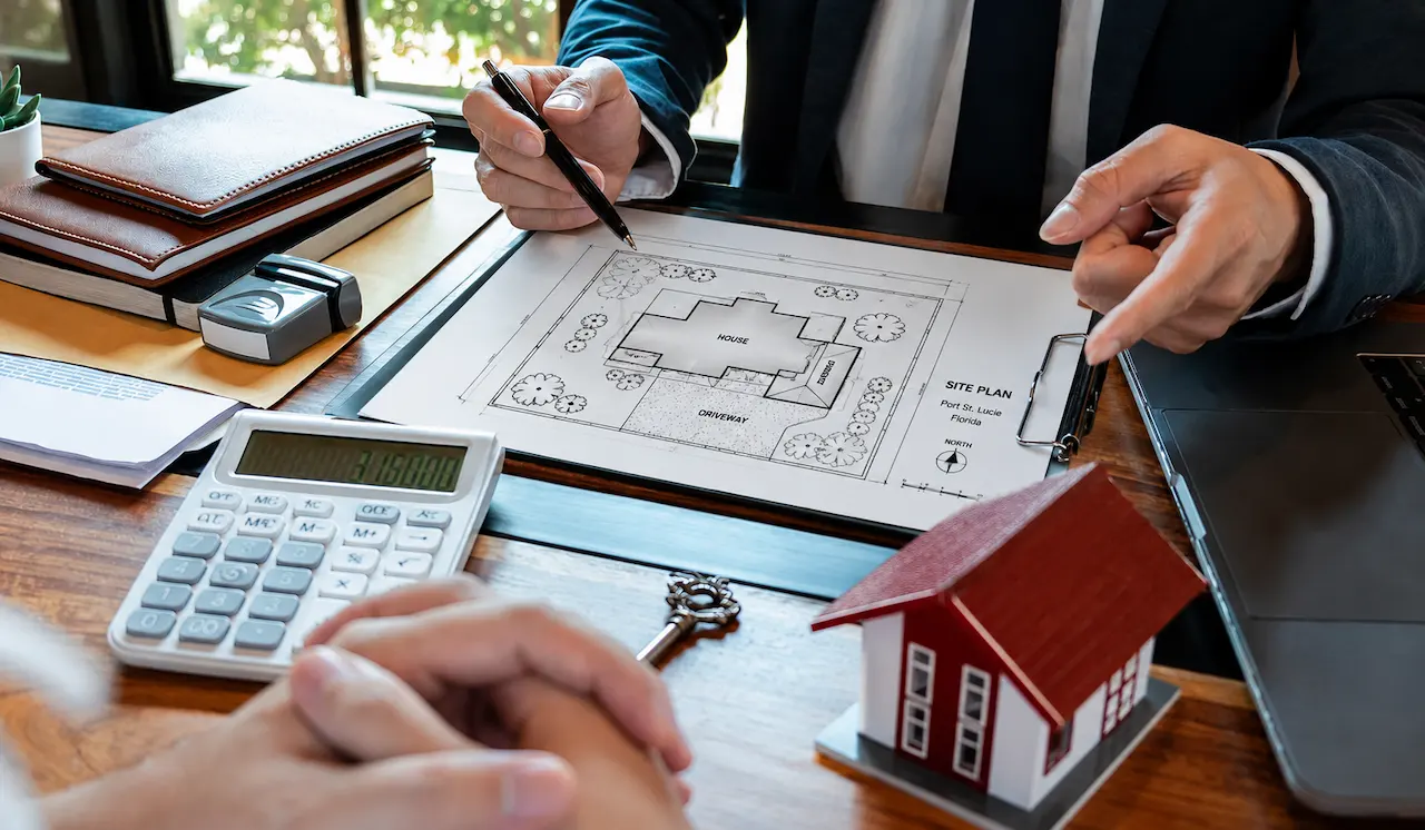 Architect reviewing a residential site plan for a permit in Port St. Lucie, Florida, with a property layout, calculator, model house, and planning documents on a desk